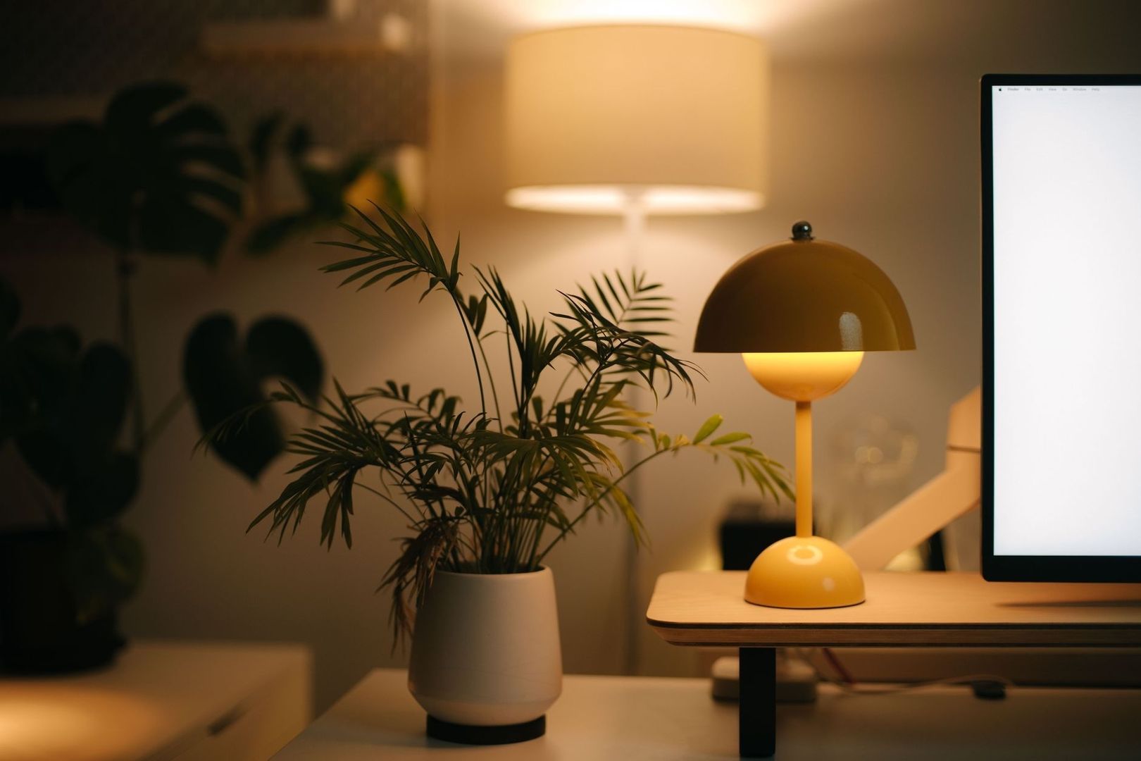 Varmt belyst hemmakontor med skrivbordslampa, växt och skärm