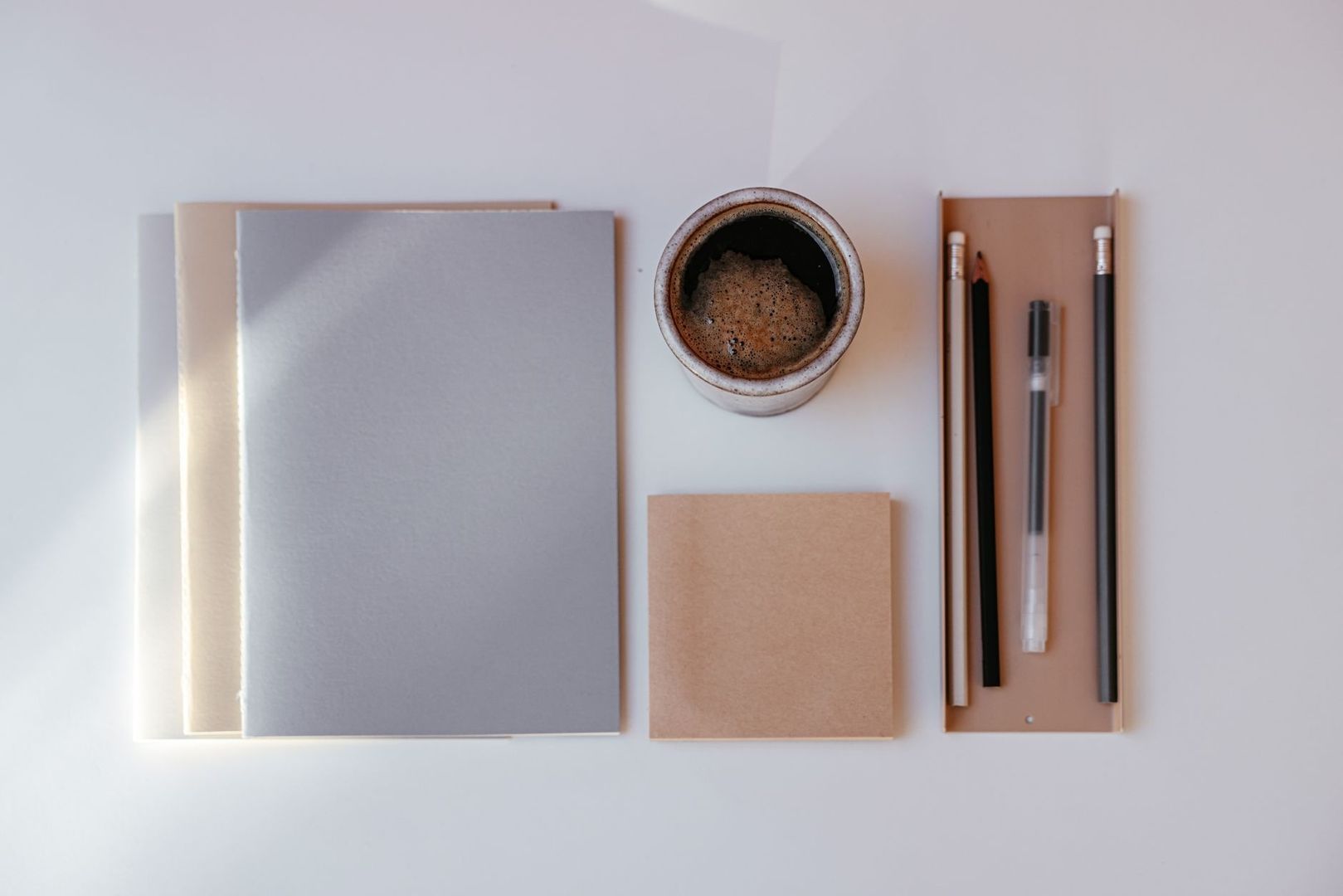 Minimalistiskt skrivbord med anteckningsböcker, kaffe och pennor